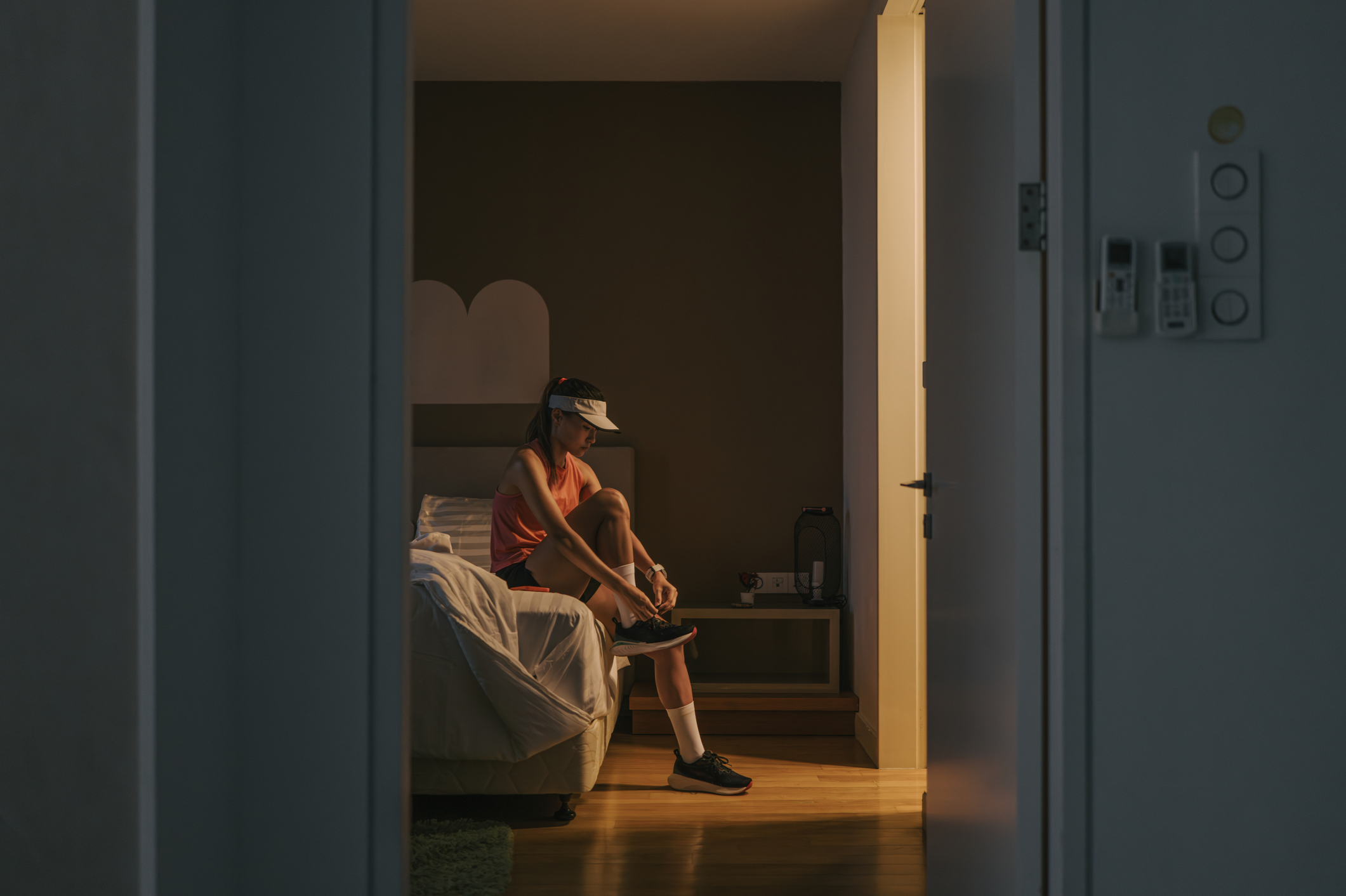 Woman tying running shoes in dim hallway at dawn